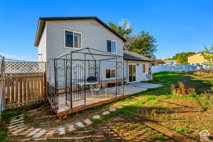 Two-story exterior with light-colored horizontal siding, elevated wood deck, wrought-iron gazebo frame, sliding glass door, and perimeter privacy fencing