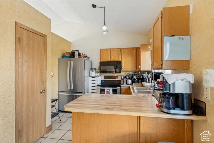 Kitchen featuring wood cabinetry, laminate countertops, stainless steel appliances, tiled flooring, and a vaulted ceiling with a pendant light fixture