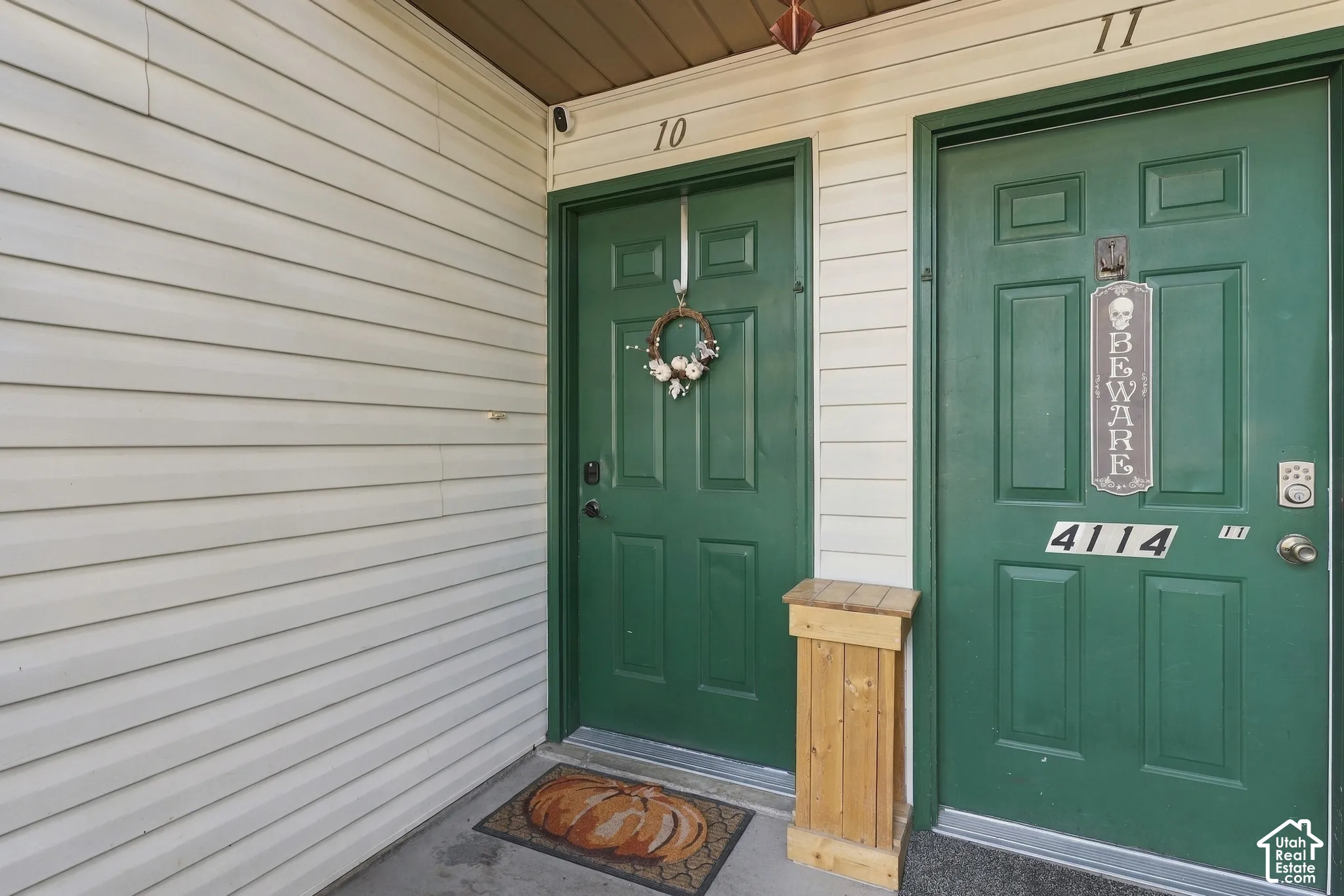 Exterior entry featuring light-colored horizontal siding, dual green paneled doors, and numerical address signage