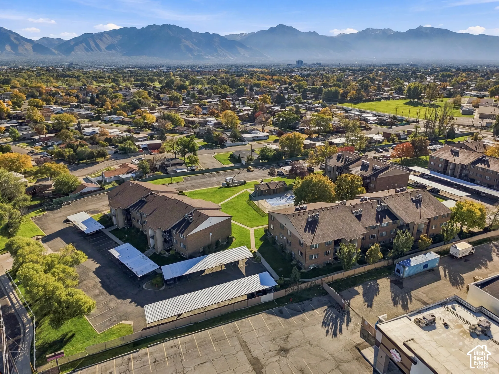 Aerial perspective of multi-building property featuring a central courtyard, swimming pool, shaded parking structures, and mountain backdrop