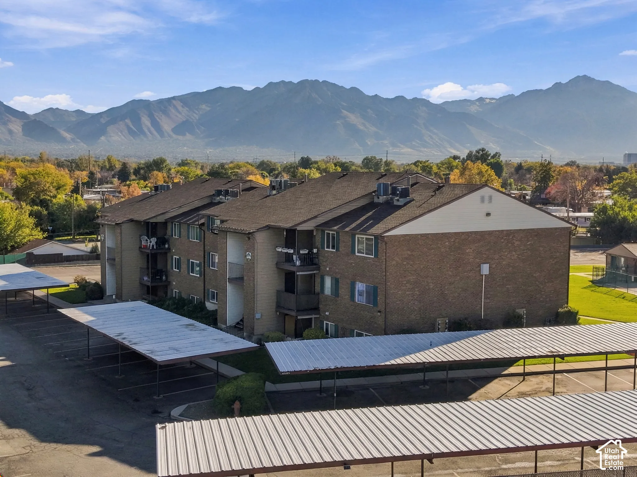 Multi-story brick building exterior featuring private balconies and covered parking structures against a mountain backdrop