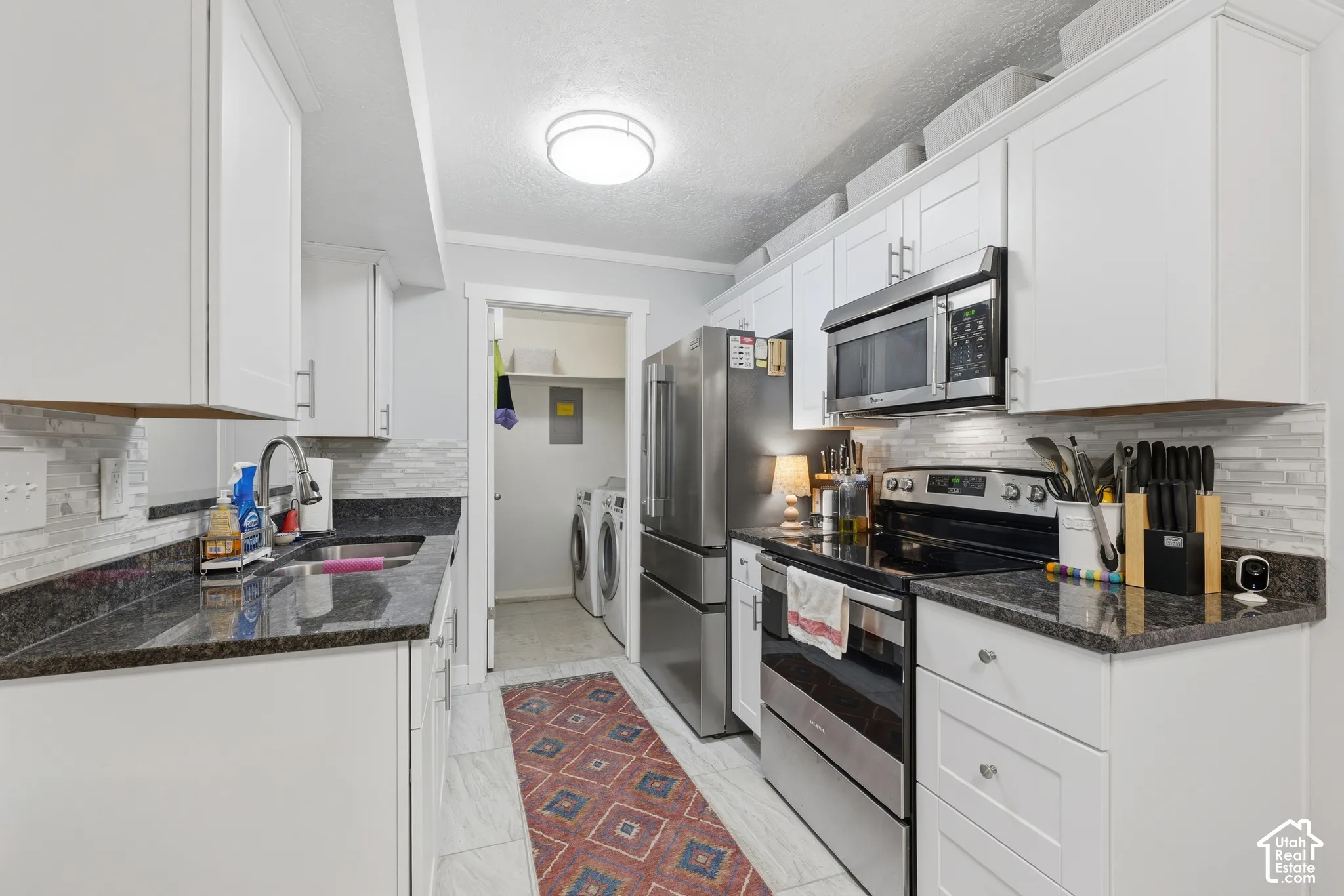 Kitchen featuring white shaker-style cabinetry, dark stone-finish countertops, stainless steel appliances, and a horizontal tile backsplash