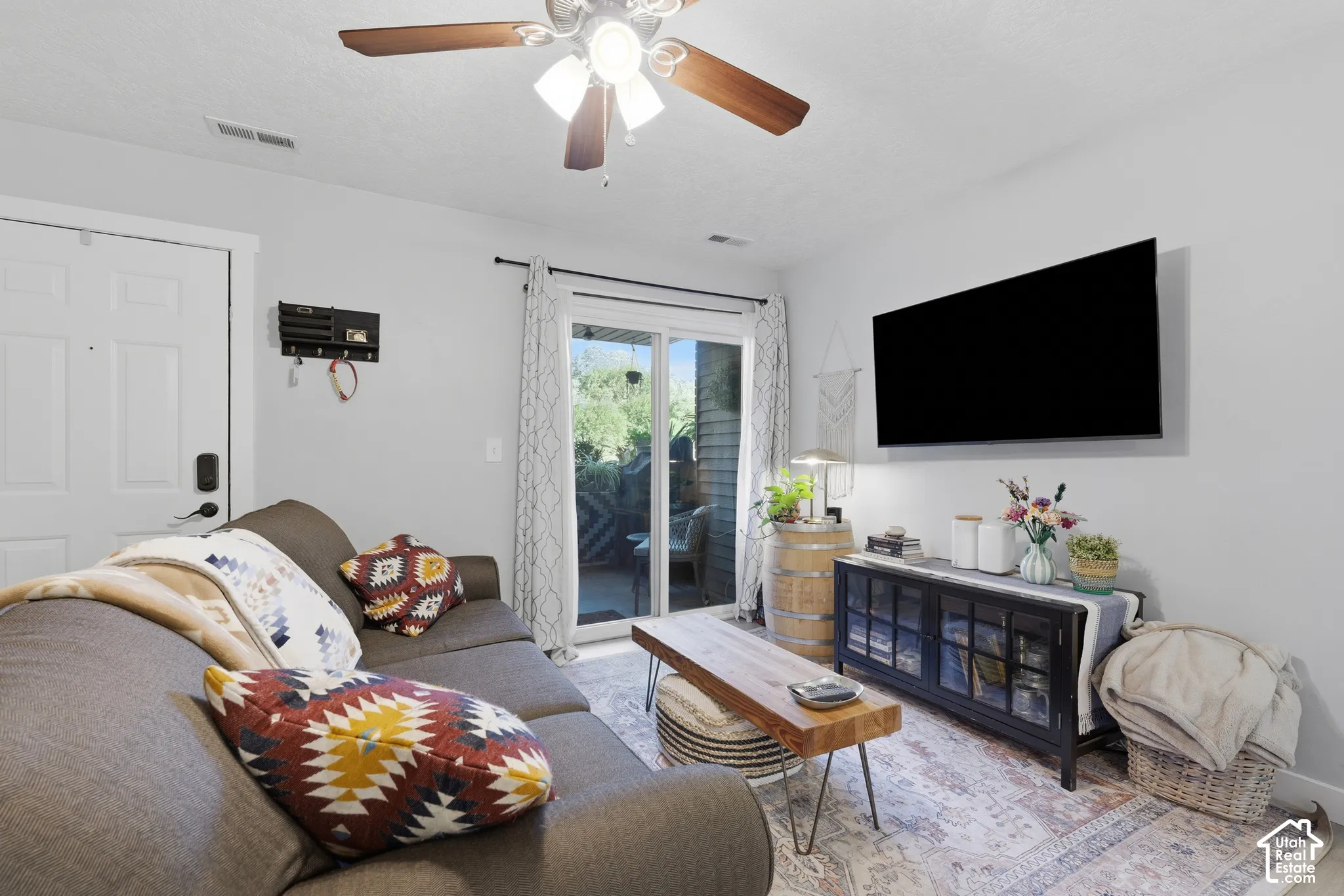 Living area featuring a ceiling fan with integrated lighting, glass sliding doors, and a wall-mounted television