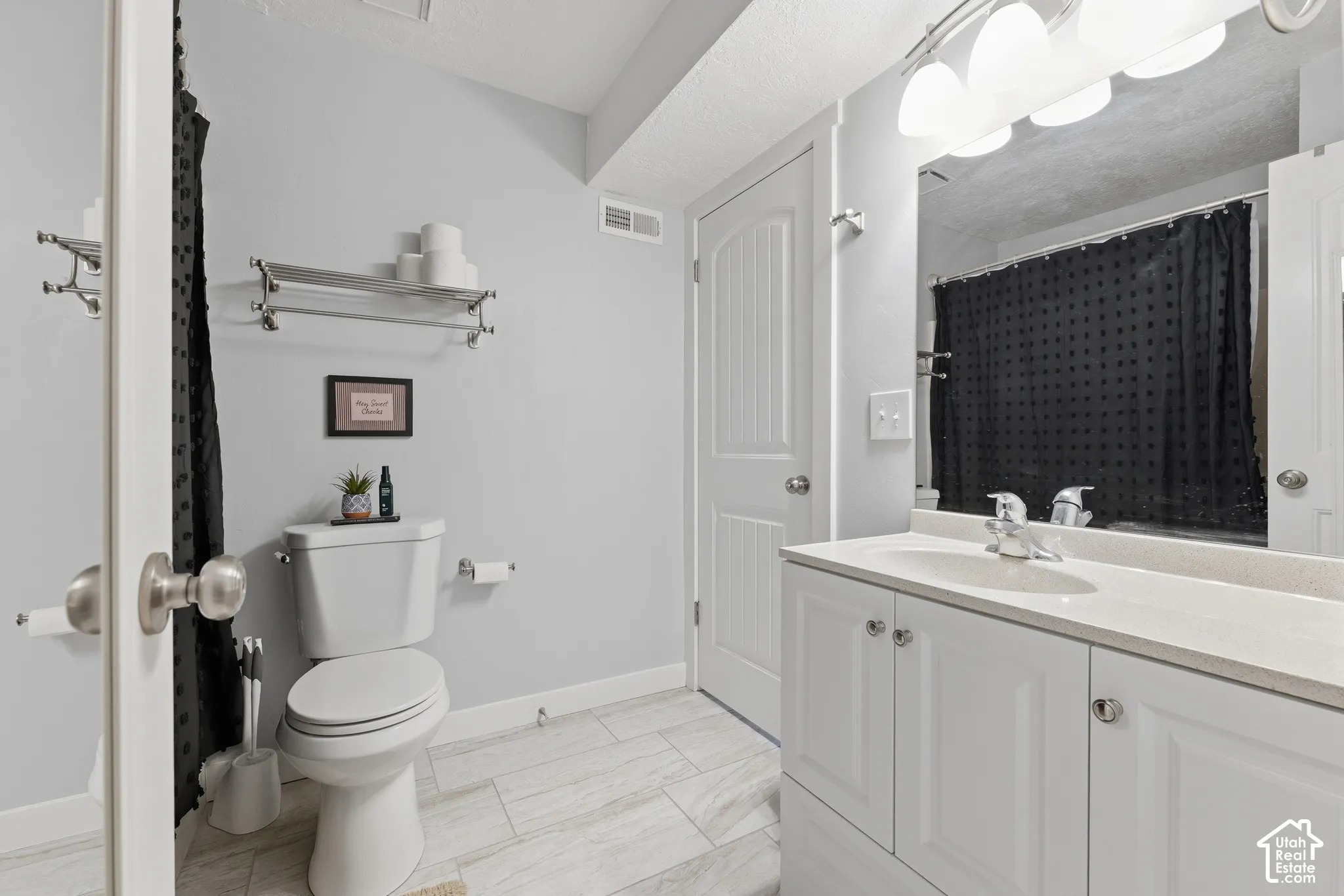 Bathroom featuring a white vanity cabinet with an integrated countertop, polished chrome faucet, full-width mirror, and tile flooring