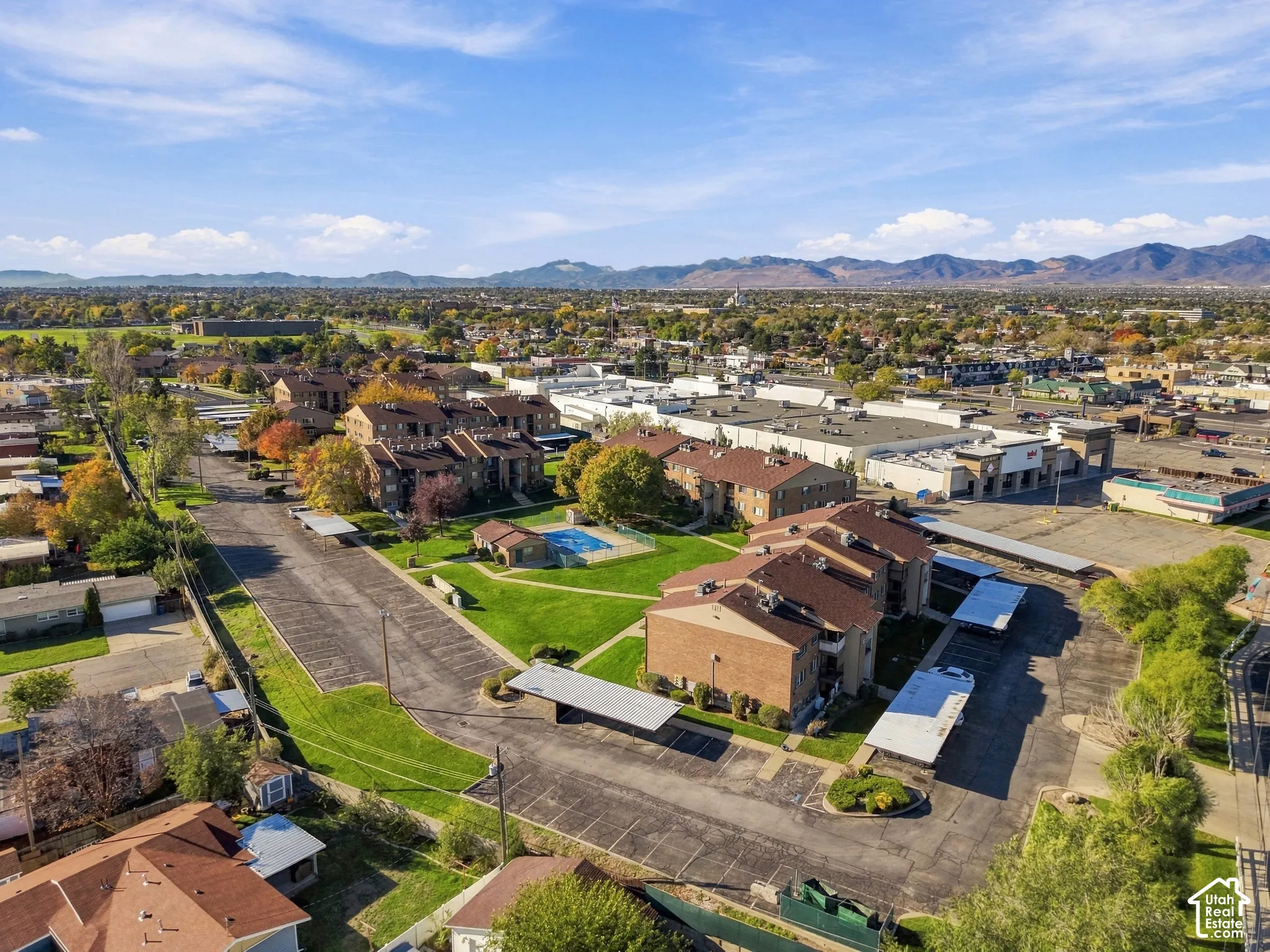 Aerial perspective of multi-family brick structures featuring covered parking, open green space, a swimming pool, and a mountain backdrop