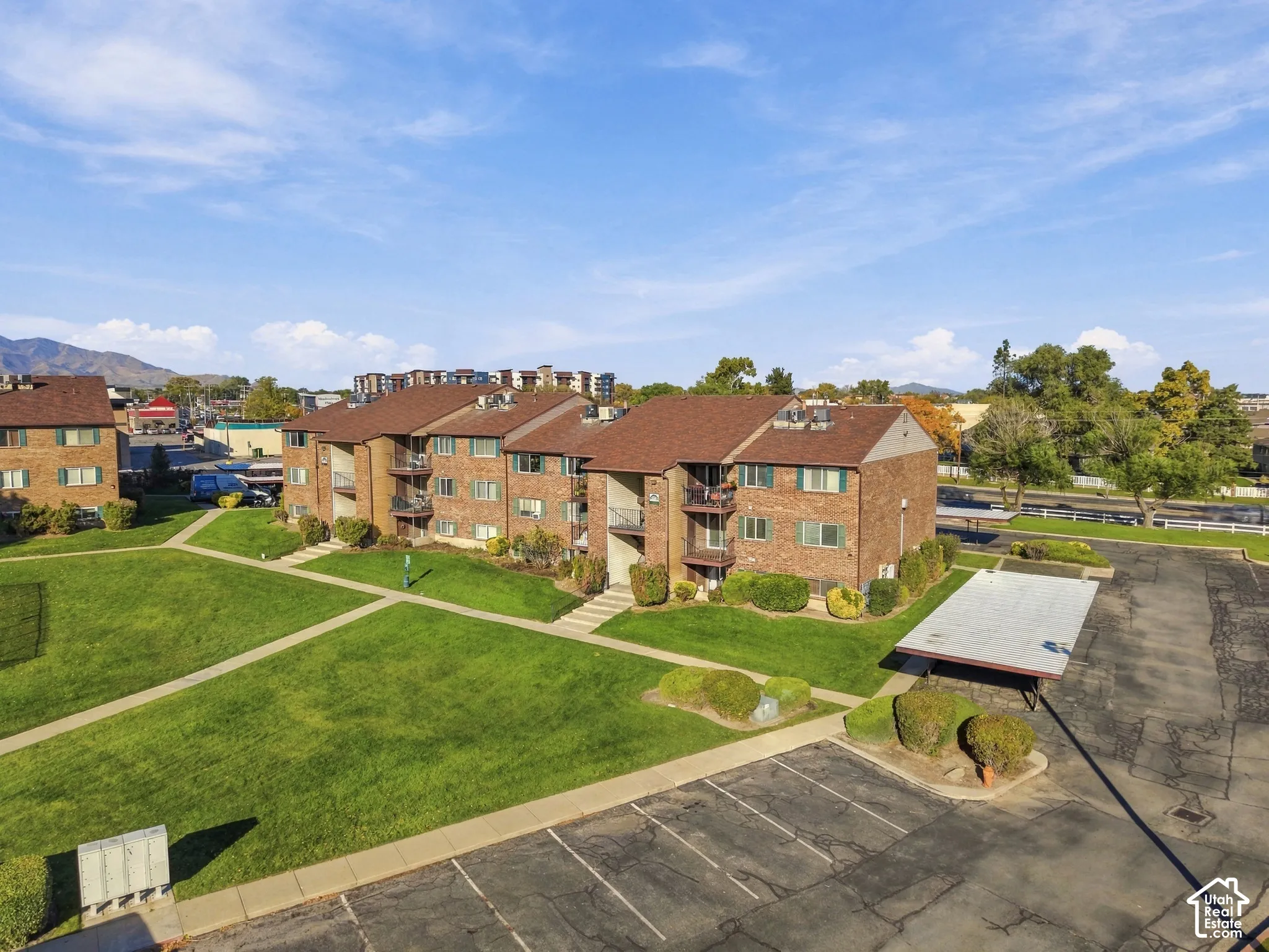 Multi-story brick exterior featuring asphalt shingle roofing, private balconies, expansive lawn space, and dedicated covered parking