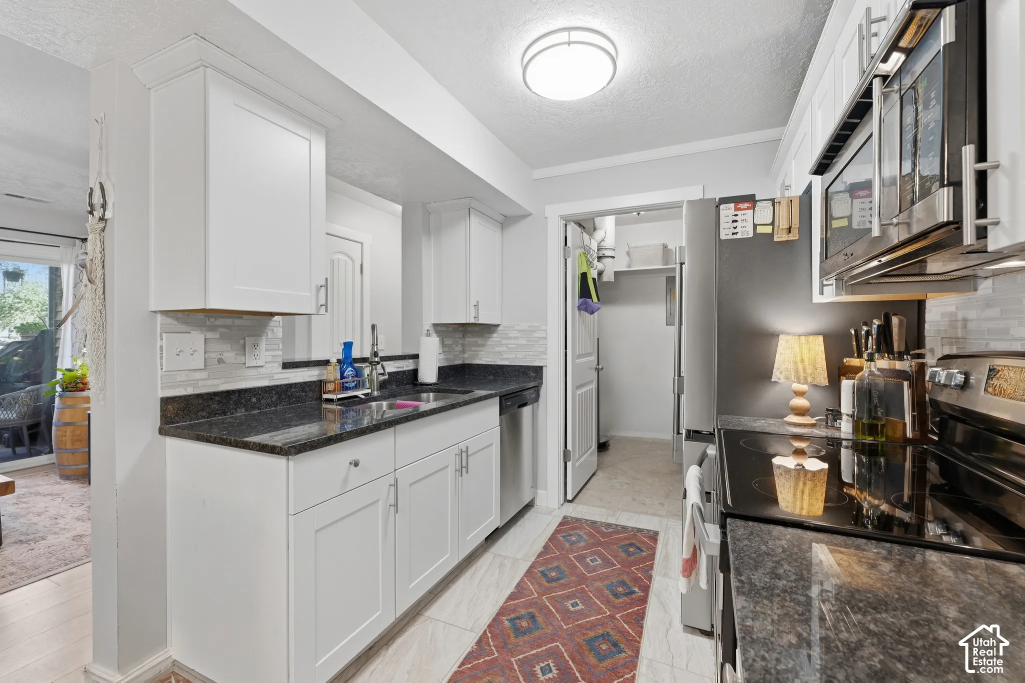 Kitchen featuring white shaker-style cabinetry, dark stone countertops, stainless steel appliances, and a tiled backsplash