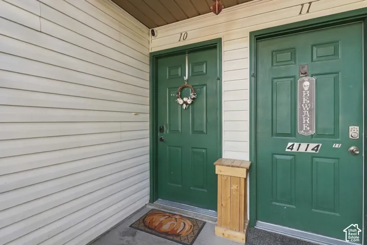 Exterior entry featuring light-colored horizontal siding, dual green paneled doors, and numerical address signage