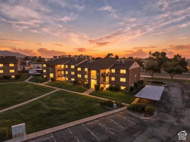 Multi-story brick exterior building featuring paved parking areas, covered parking structures, manicured lawn spaces, and concrete walkways