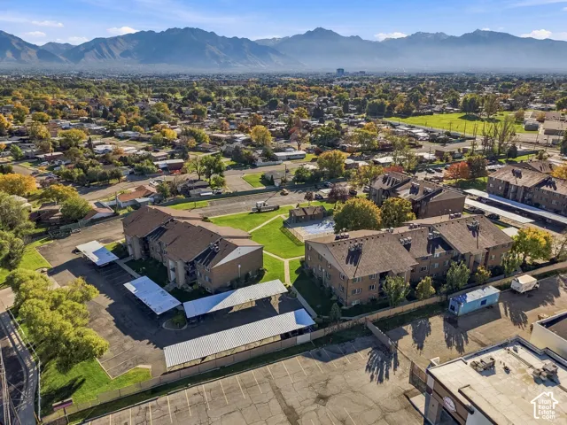 Aerial perspective of multi-building property featuring a central courtyard, swimming pool, shaded parking structures, and mountain backdrop