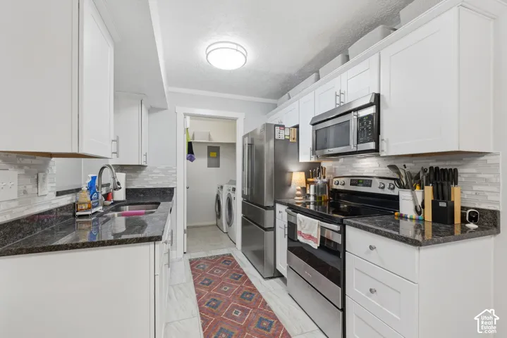 Kitchen featuring white shaker-style cabinetry, dark stone-finish countertops, stainless steel appliances, and a horizontal tile backsplash