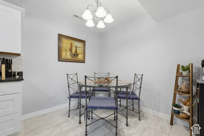 Dining area featuring a multi-bulb chandelier, light-toned tile flooring, and white shaker-style cabinetry with dark countertops