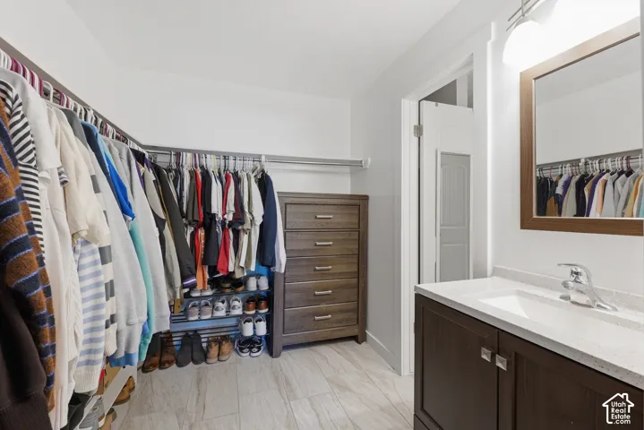 Vanity with a solid-surface countertop and integrated sink, stone-finish tile flooring, and integrated closet organization system with hanging rods