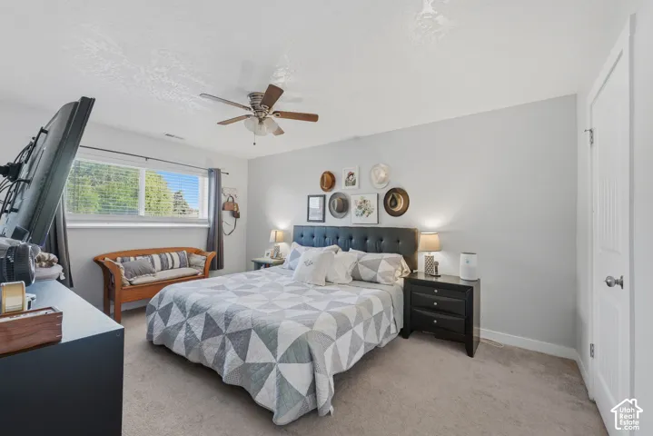 Neutral interior room featuring carpeted flooring, a ceiling fan with integrated lighting, a sliding window with horizontal blinds, and a multi-panel door