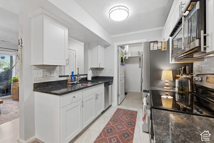 Kitchen featuring white shaker-style cabinetry, dark stone countertops, stainless steel appliances, and a tiled backsplash