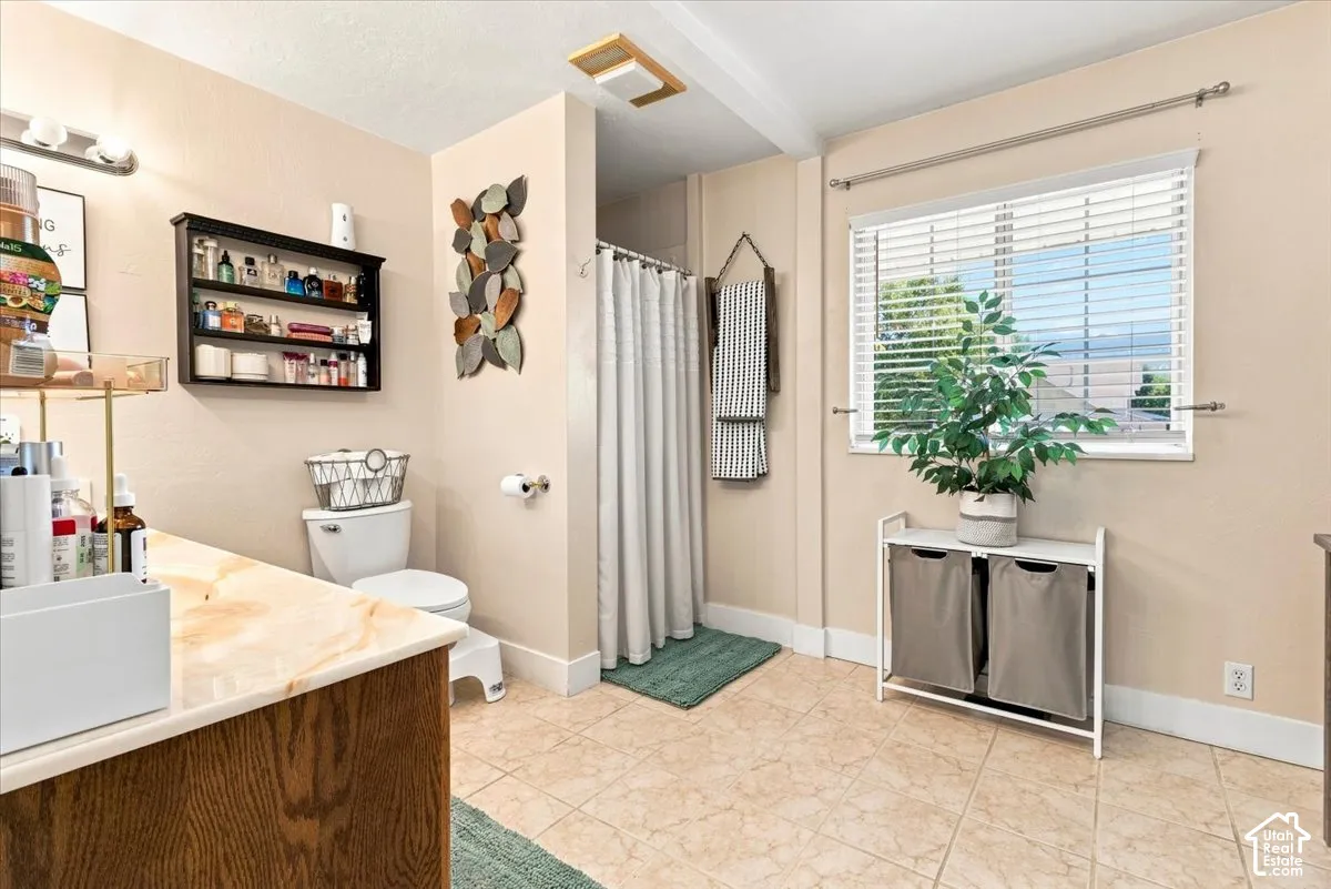 Bathroom featuring a stone-top vanity, ceramic tile flooring, horizontal window blinds, and a built-in wall shelf