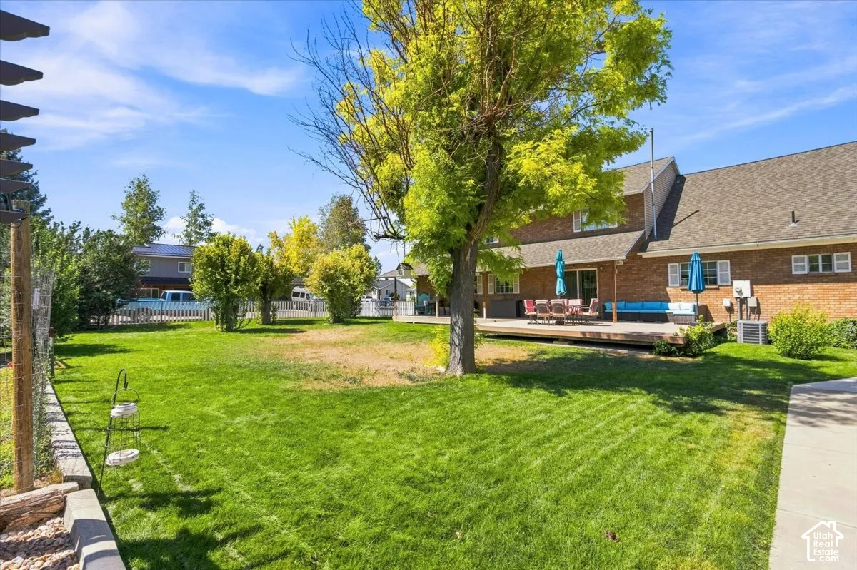 Expansive backyard featuring a brick exterior, elevated wood deck, mature trees, and a concrete walkway