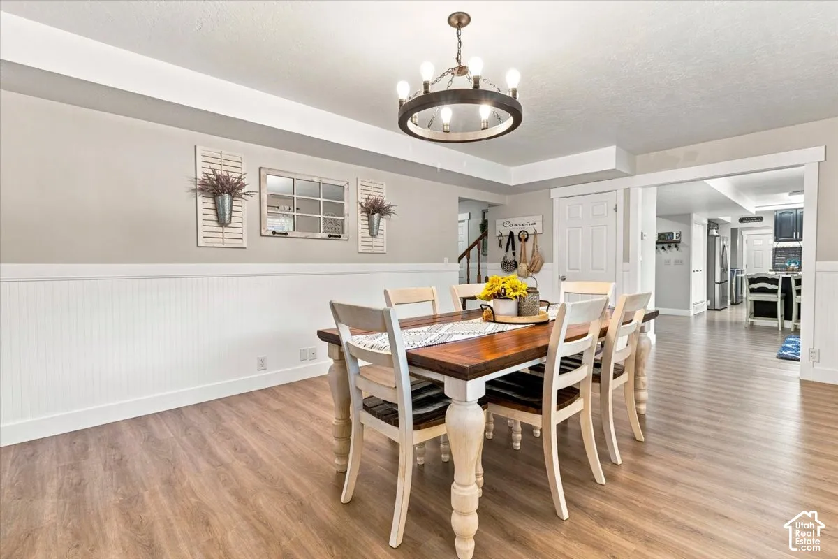 Dining area featuring wood-finish flooring, white beadboard wainscoting, and a circular wagon wheel-style chandelier with exposed bulbs
