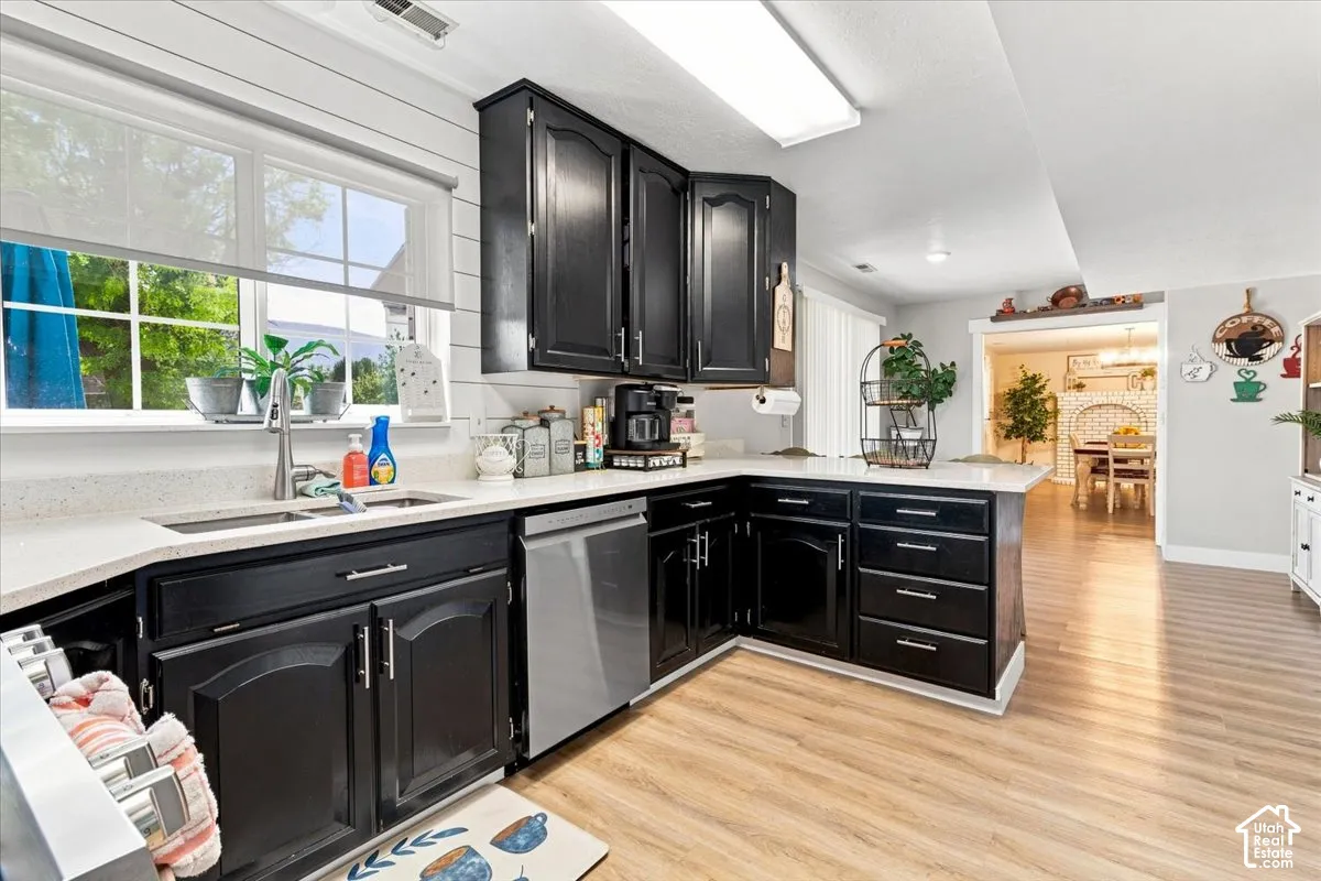 Kitchen featuring dark cabinetry, solid-surface countertops, wood-finish flooring, stainless steel dishwasher, and horizontal wall paneling