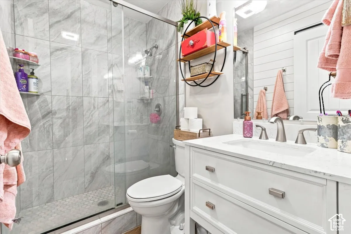Bathroom featuring a white vanity with a stone countertop, an integrated sink, polished metal fixtures, a glass-enclosed shower with large-format tile surround, and horizontal wall paneling