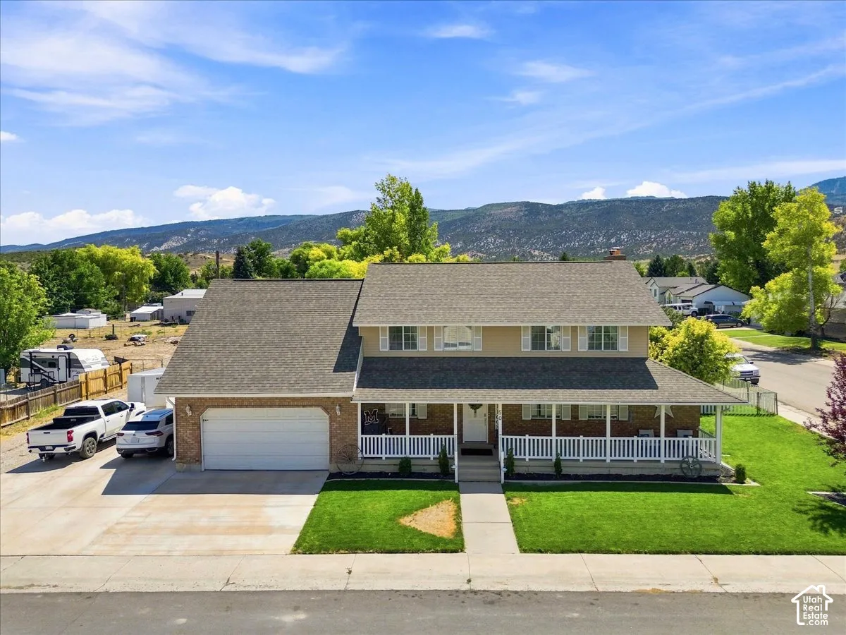 Two-story residence featuring brick and siding exterior, a covered wrap-around front porch, an attached garage, and mountain scenery