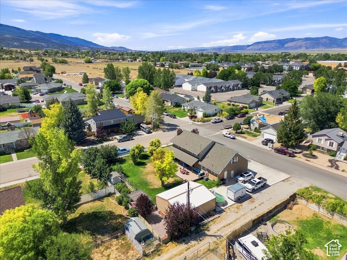 Aerial view featuring a two-story residence with a concrete patio, a detached garage, and a fenced yard with mature trees, set against a mountain backdrop