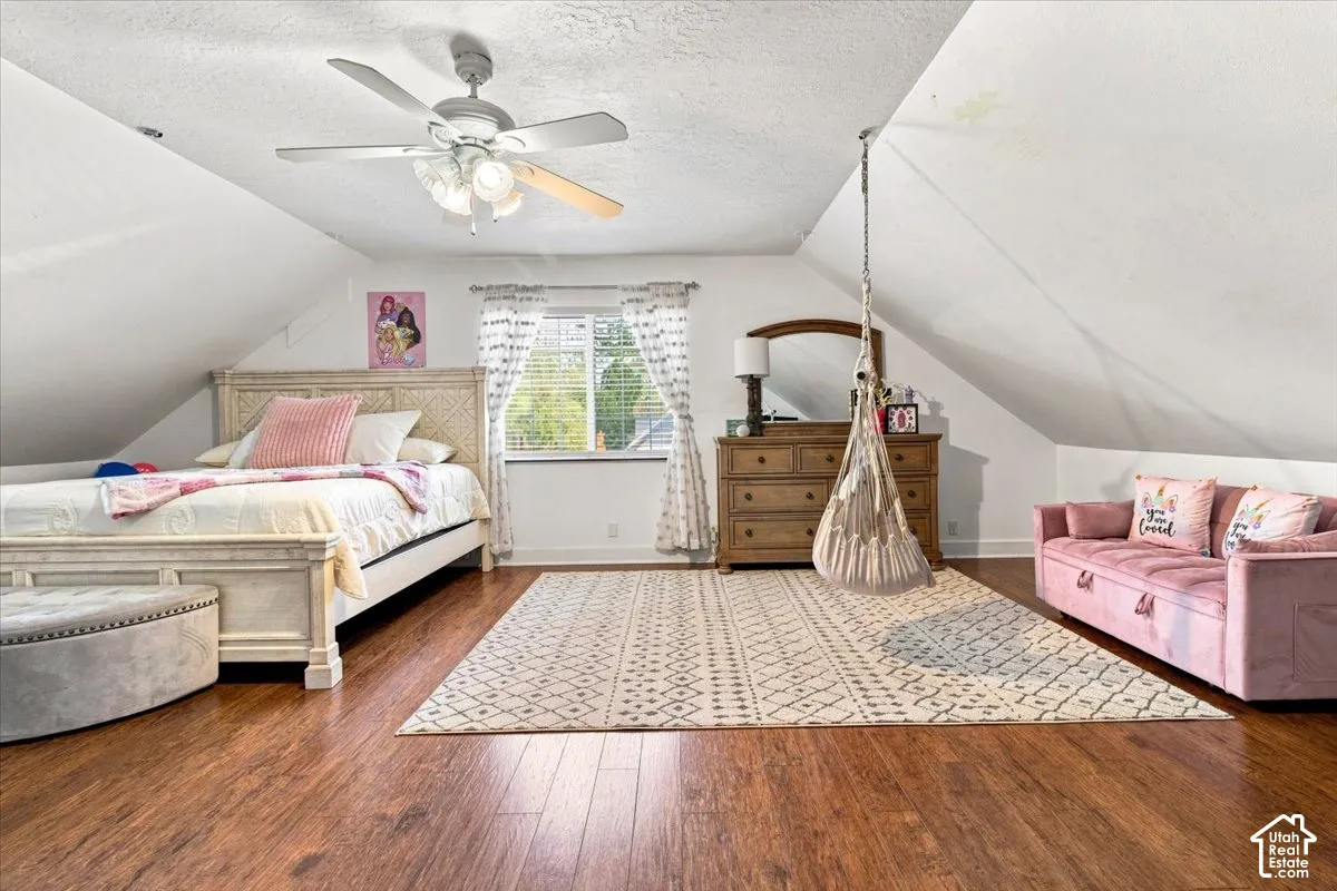 Vaulted ceiling featuring a central white ceiling fan with integrated lighting, wood-finish flooring, and a window with natural light