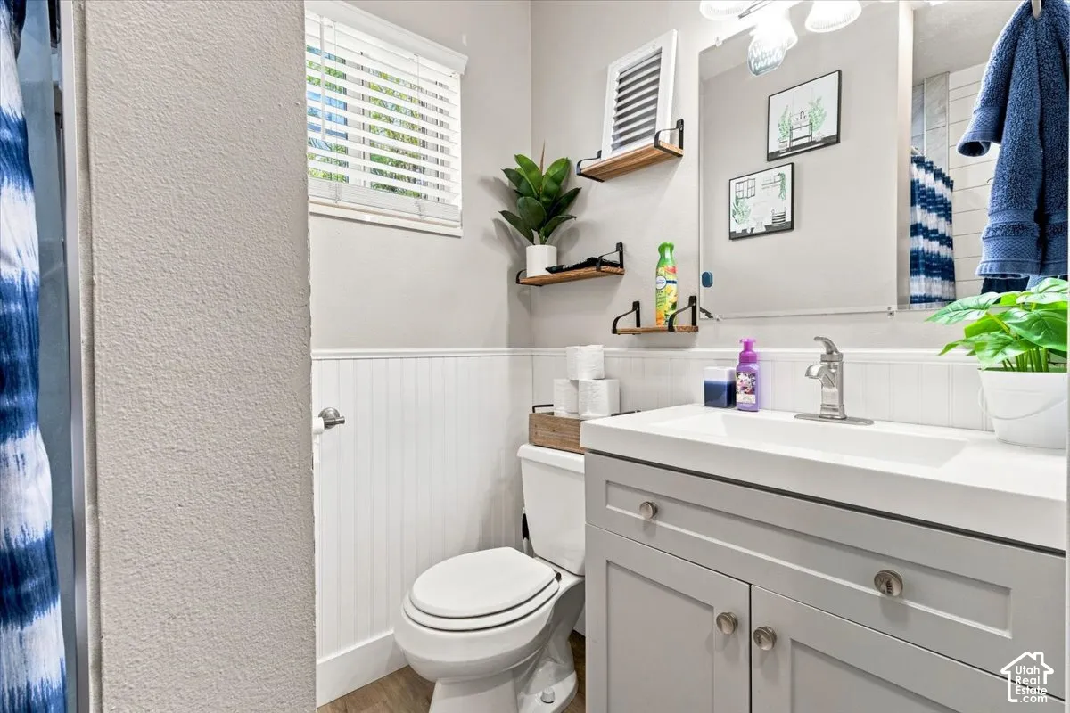 Bathroom featuring a gray vanity with an integrated rectangular sink, beadboard wainscoting, polished chrome faucet, wall-mounted wood shelving, and a large plate glass mirror