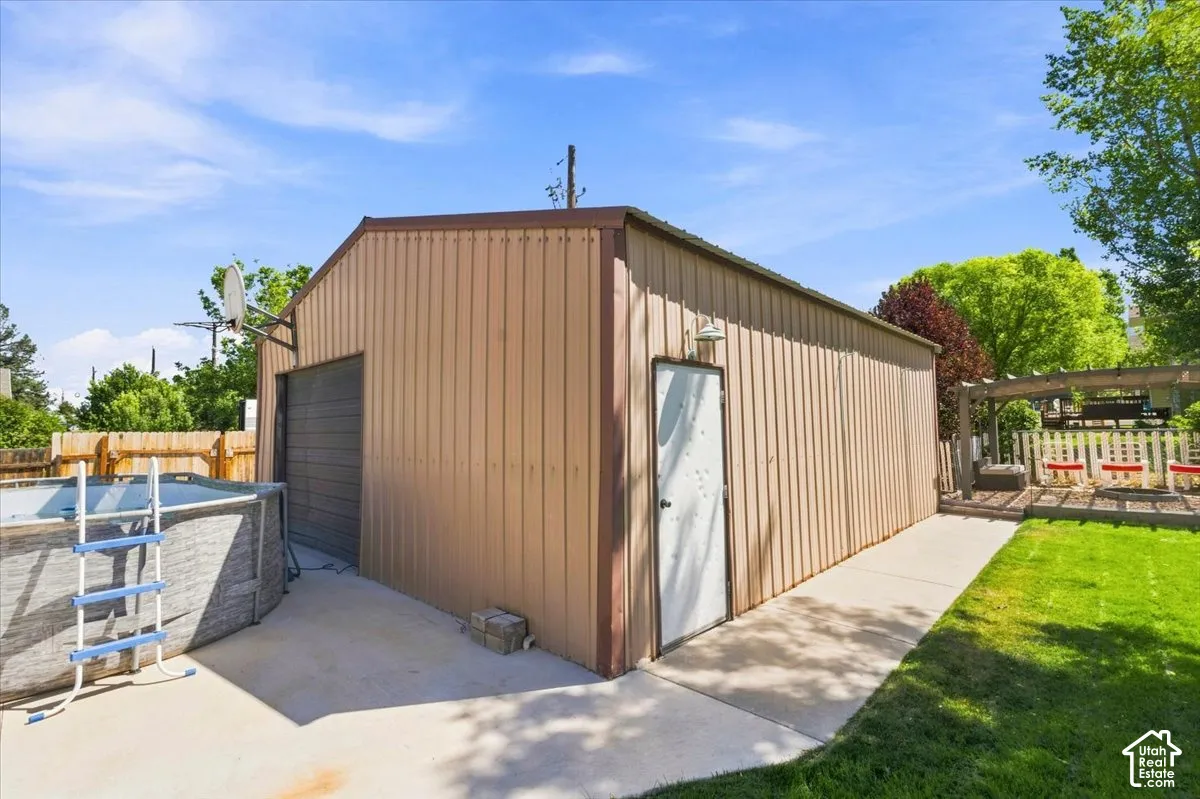 Detached metal-sided garage featuring a concrete apron, single-entry door, and attached exterior lighting