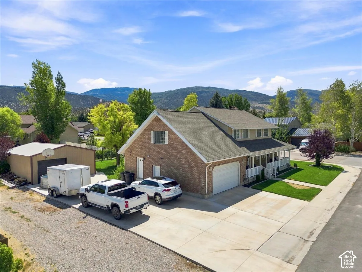 Two-story brick exterior featuring a covered front porch, an attached two-car garage, a detached storage structure, and mountain backdrop