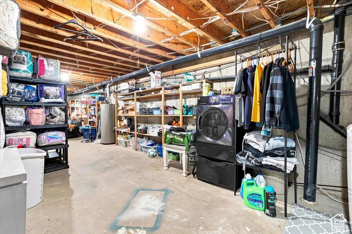 Unfinished lower level featuring exposed joist ceiling, concrete flooring, built-in wooden shelving, and dedicated laundry connections