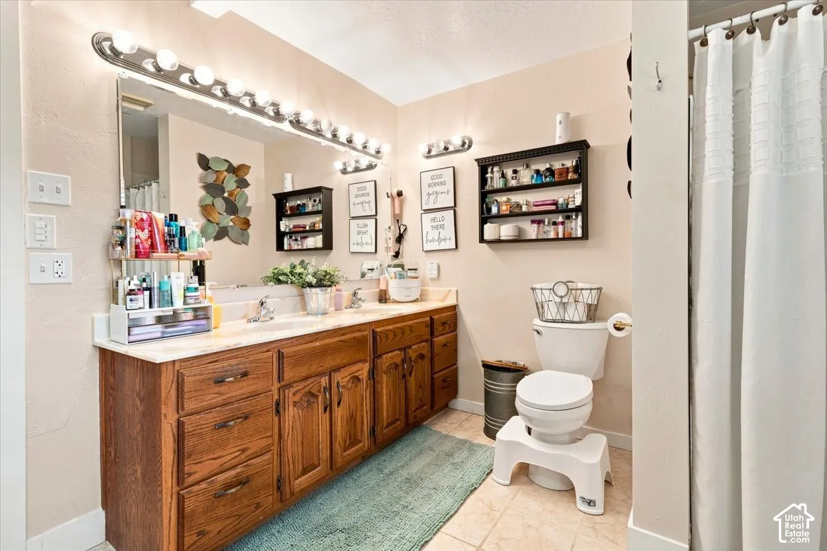 Double-vanity bathroom featuring wood cabinetry, a full-width vanity mirror, two wall-mounted light fixtures, and a dual-basin countertop