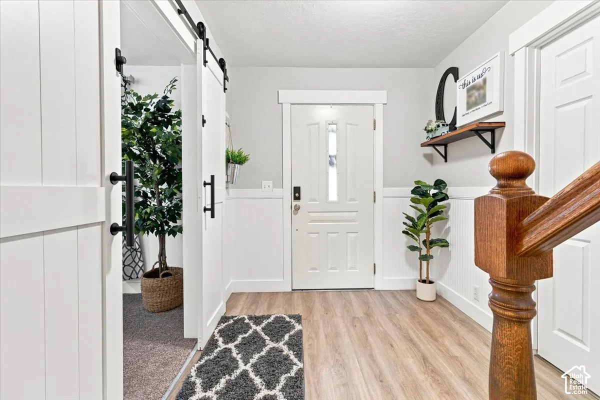 Entry featuring white beadboard wainscoting, wood-finish flooring, a sliding white barn door, and a wooden staircase newel post