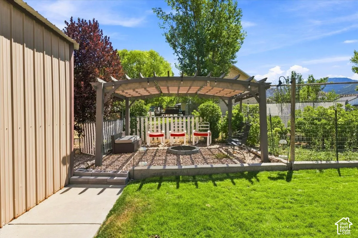 Backyard featuring a custom pergola, a stone-lined fire pit area, concrete walkway, and a manicured lawn