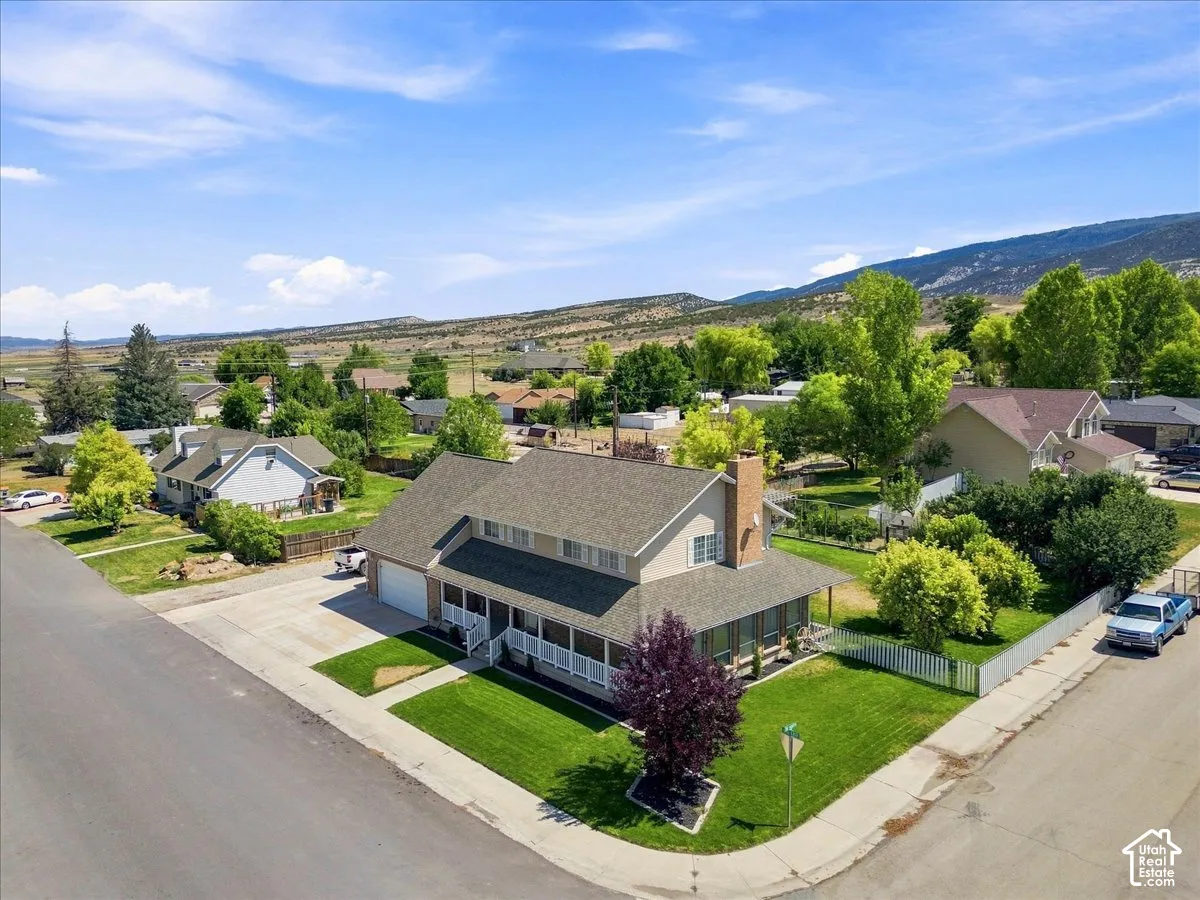 Two-story residence featuring a covered wrap-around porch, attached two-car garage, exterior chimney, and a corner lot configuration with mountain scenery