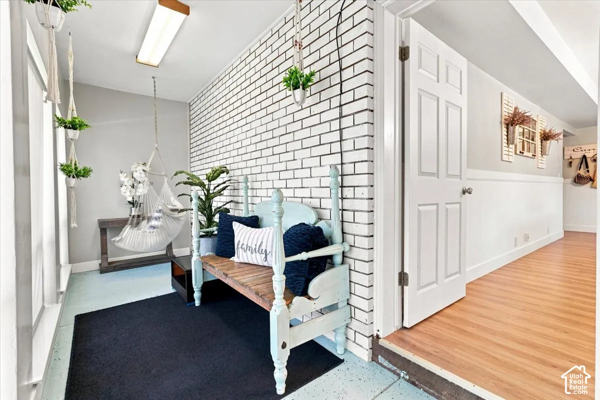 Interior space featuring a painted white brick wall, wood-finish flooring, white panel door, and wainscoting