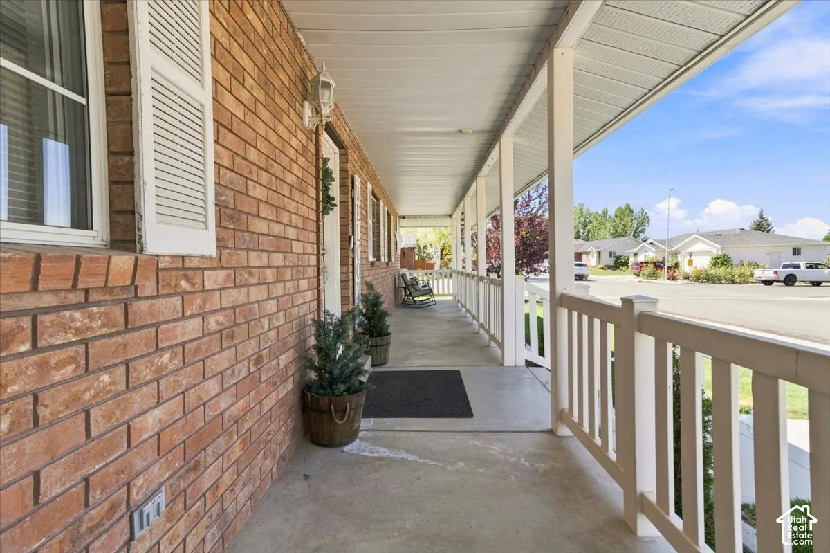 Covered front porch featuring a brick exterior, concrete flooring, and a white picket-style railing