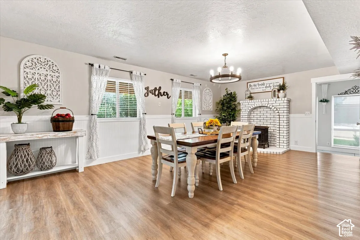 Dining space featuring wood-finish flooring, white wainscoting, an arched brick fireplace, a rustic circular chandelier, and built-in wall decor