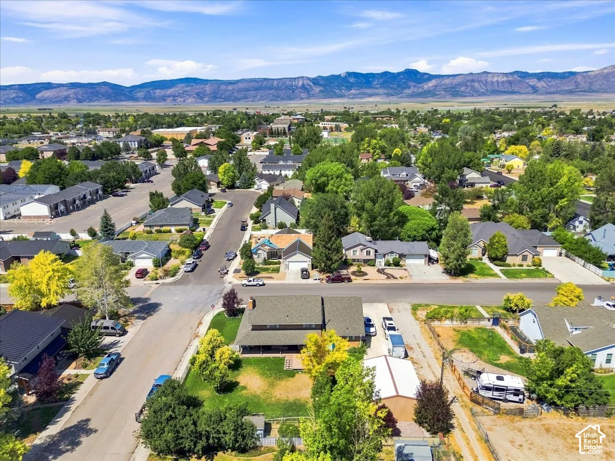 Aerial perspective featuring a multi-story residence with a multi-gabled roof, expansive green lawn, mature trees, and prominent mountain range backdrop