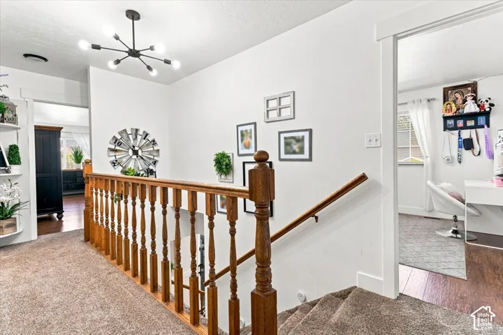 Staircase featuring a wooden banister with turned spindles, overhead multi-arm modern light fixture, and neutral carpeting