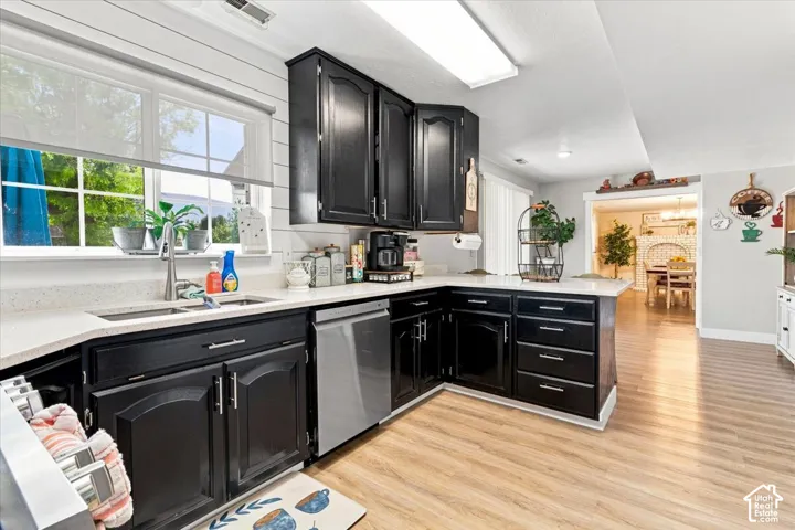 Kitchen featuring dark cabinetry, solid-surface countertops, wood-finish flooring, stainless steel dishwasher, and horizontal wall paneling