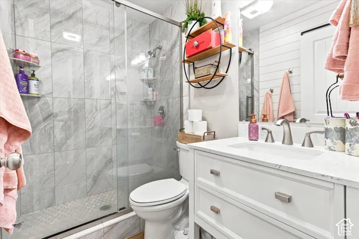 Bathroom featuring a white vanity with a stone countertop, an integrated sink, polished metal fixtures, a glass-enclosed shower with large-format tile surround, and horizontal wall paneling