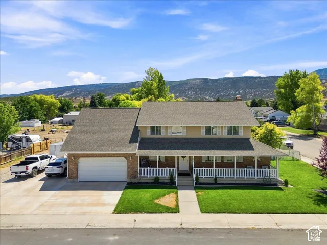 Two-story residence featuring brick and siding exterior, a covered wrap-around front porch, an attached garage, and mountain scenery