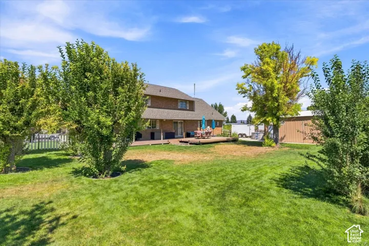 Expansive backyard featuring a manicured lawn, mature trees, a wooden deck, and a detached metal storage structure