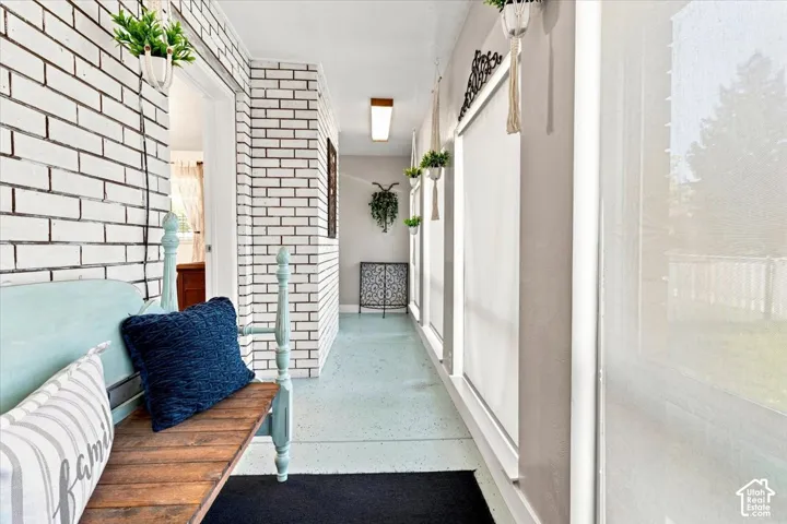 Enclosed sunroom featuring white painted brick walls, large windows, and solid-surface flooring