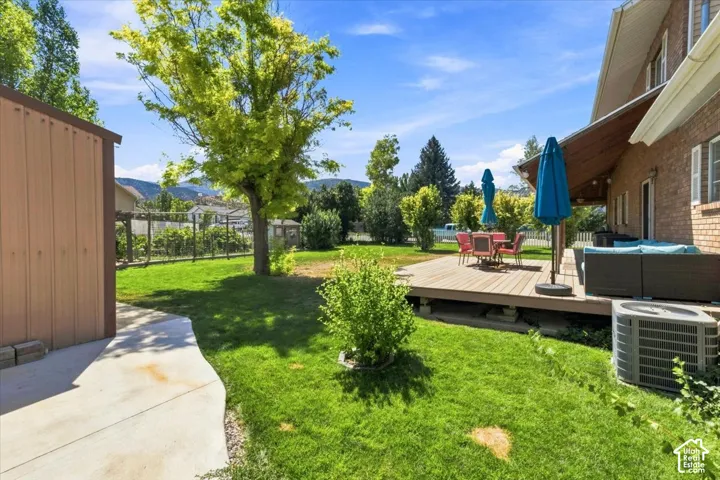 Expansive backyard featuring a wood deck, concrete patio, mature trees, and mountain backdrop