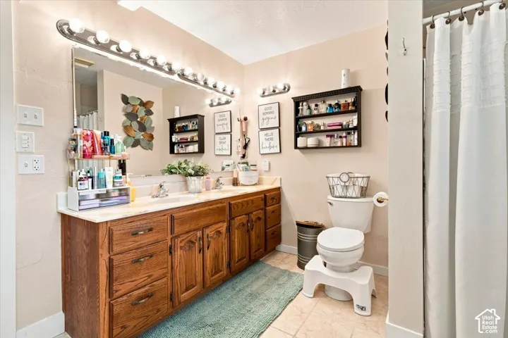 Double-vanity bathroom featuring wood cabinetry, a full-width vanity mirror, two wall-mounted light fixtures, and a dual-basin countertop