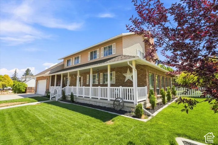 Two-story residence featuring a brick and siding exterior, a full-length covered front porch with white railing, and an attached two-car garage