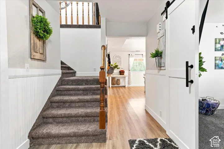Entryway featuring a white sliding barn door, beadboard wainscoting, wood-finish flooring, and a staircase with a wooden baluster