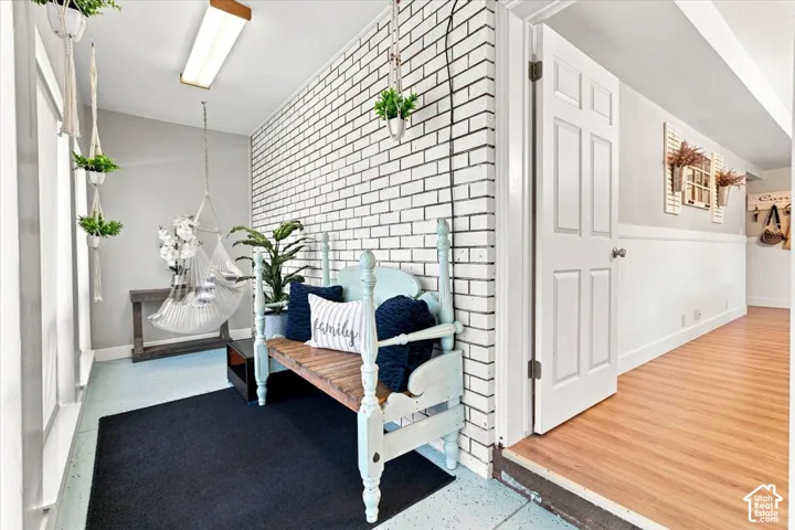 Interior space featuring a painted white brick wall, wood-finish flooring, white panel door, and wainscoting